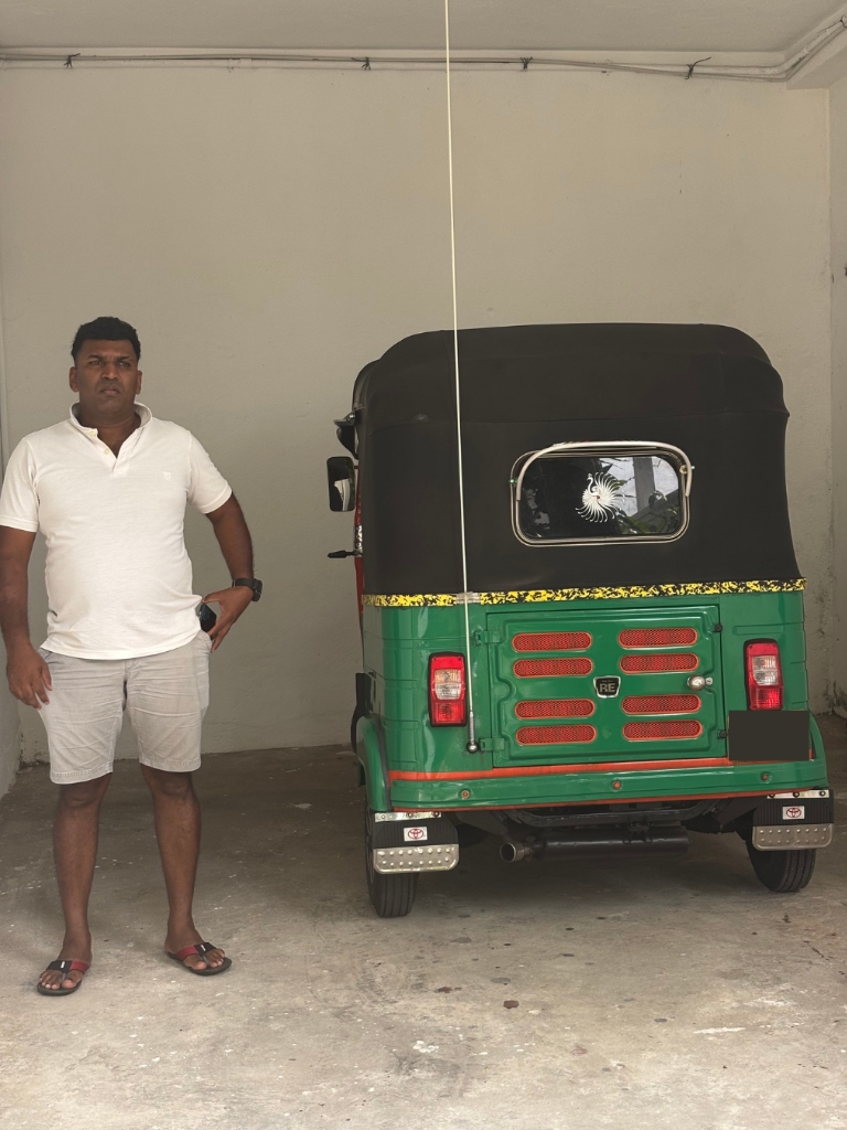 Maama standing by his custom green and orange tuk tuk